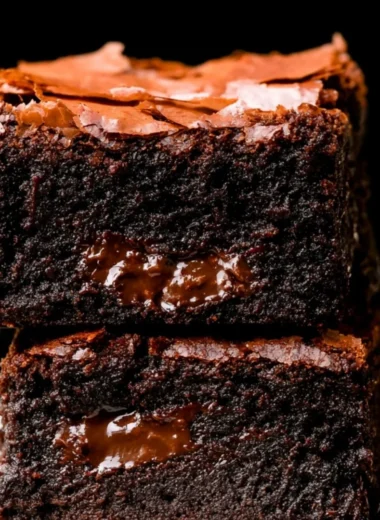Delicious fudgy brownies stacked on a wooden table, topped with chocolate drizzle.