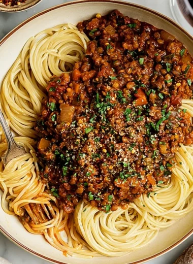 Bowl of vegan lentil bolognese served with pasta and fresh herbs