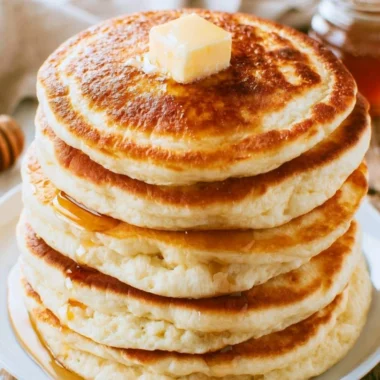 Stack of fluffy pancakes drizzled with syrup and topped with fresh berries