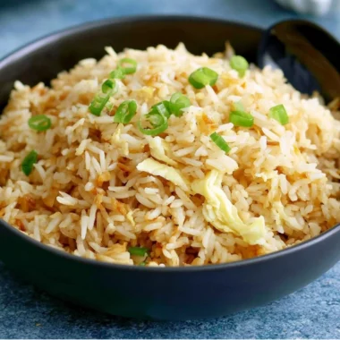 A bowl of delicious garlic fried rice garnished with green onions.