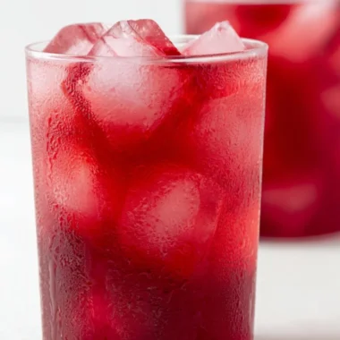 A glass of refreshing strawberry hibiscus iced tea garnished with fresh strawberries.