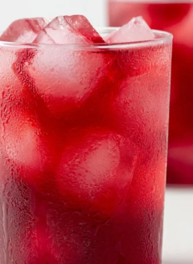 A glass of refreshing strawberry hibiscus iced tea garnished with fresh strawberries.