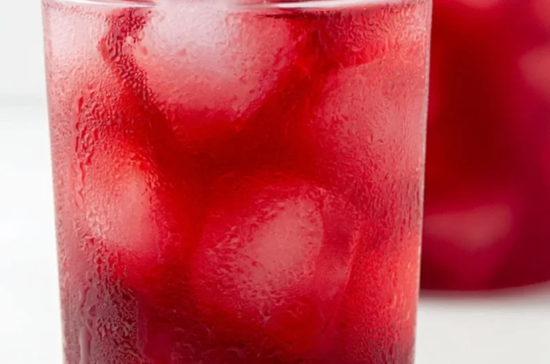 A glass of refreshing strawberry hibiscus iced tea garnished with fresh strawberries.