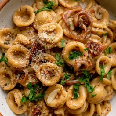 A bowl of caramelized onion pasta garnished with herbs and cheese, perfect for weeknight dinners.